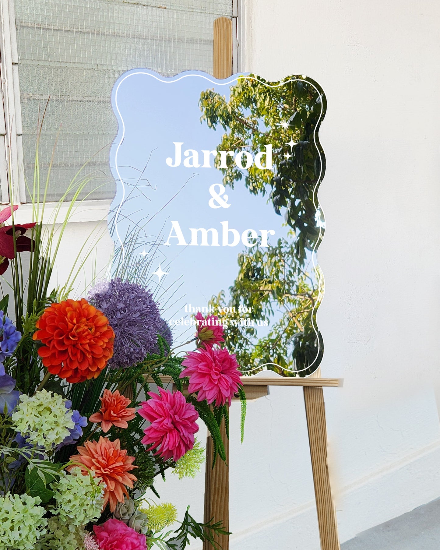 Colorful flowers on a stand with a decorative mirror and 'Jarrod & Amber' text.