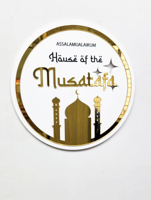 A round decorative plaque with a white background featuring Arabic calligraphy, geometric designs, and a depiction of a mosque and minaret.