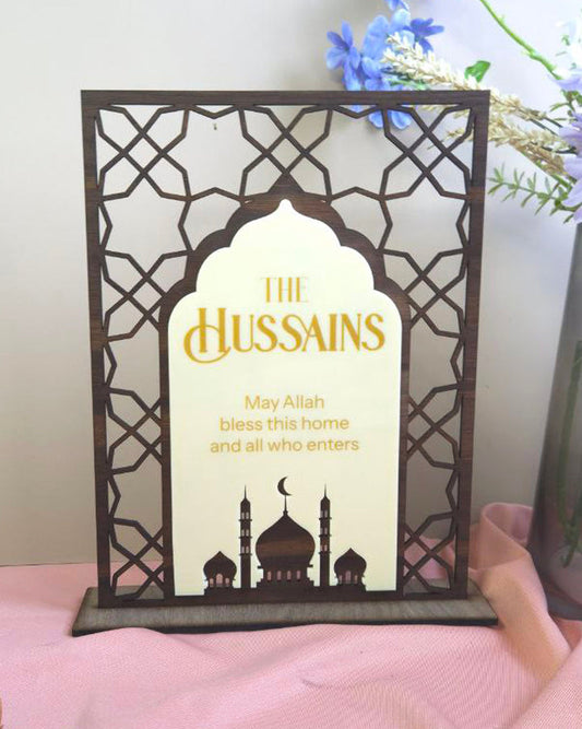 Decorative lamp with 'The Hussains' text and Islamic architectural design on a pink surface.