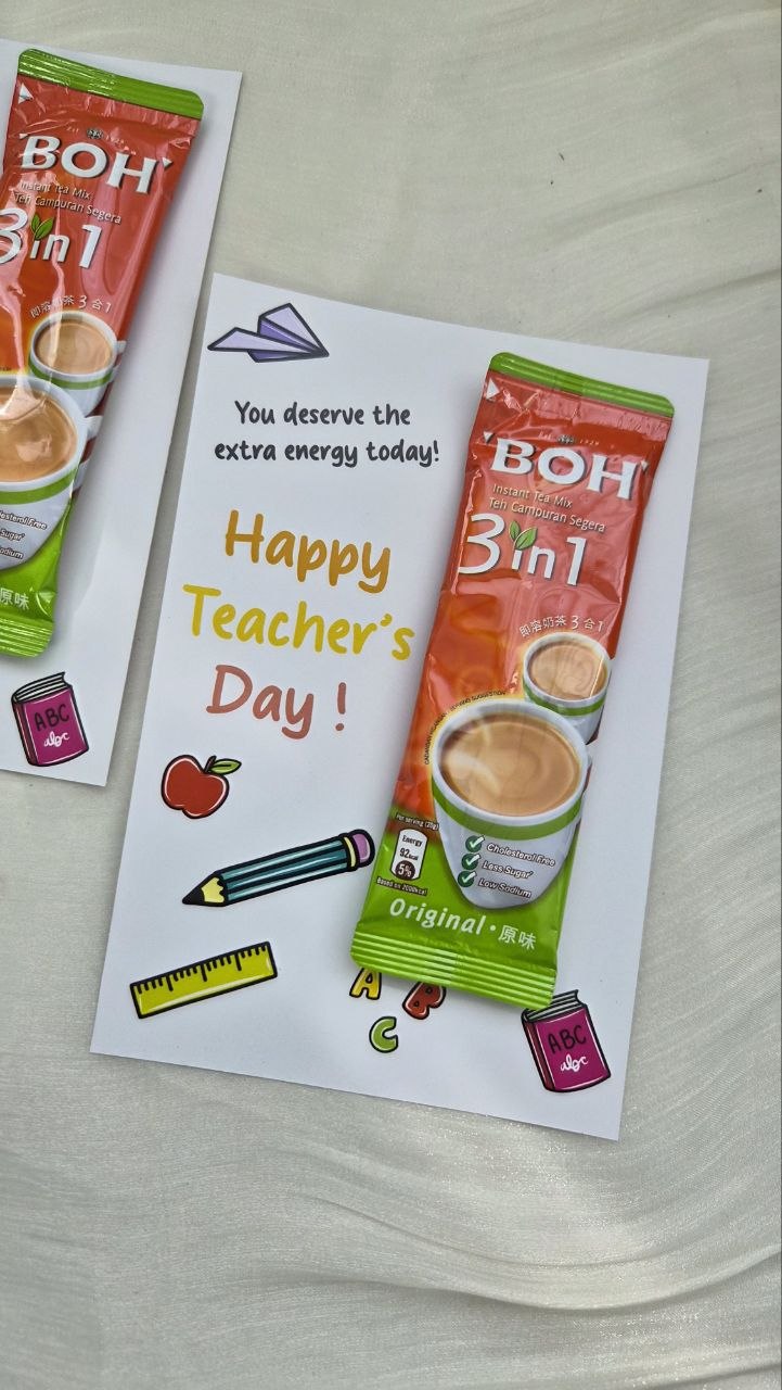 A Teacher's Day greeting card featuring a BOH 3in1 instant coffee packet illustration, with 'Happy Teacher's Day!' written in yellow text, displayed on a light fabric surface.