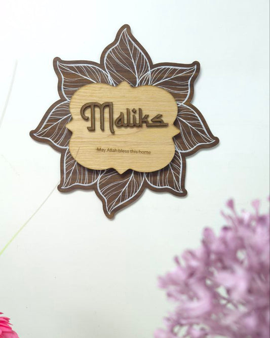 Decorative wall hanging with 'Malika' text and floral design on a white background with flowers.