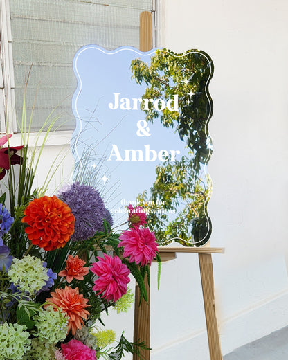 Colorful flowers on a stand with a decorative mirror and 'Jarrod & Amber' text.