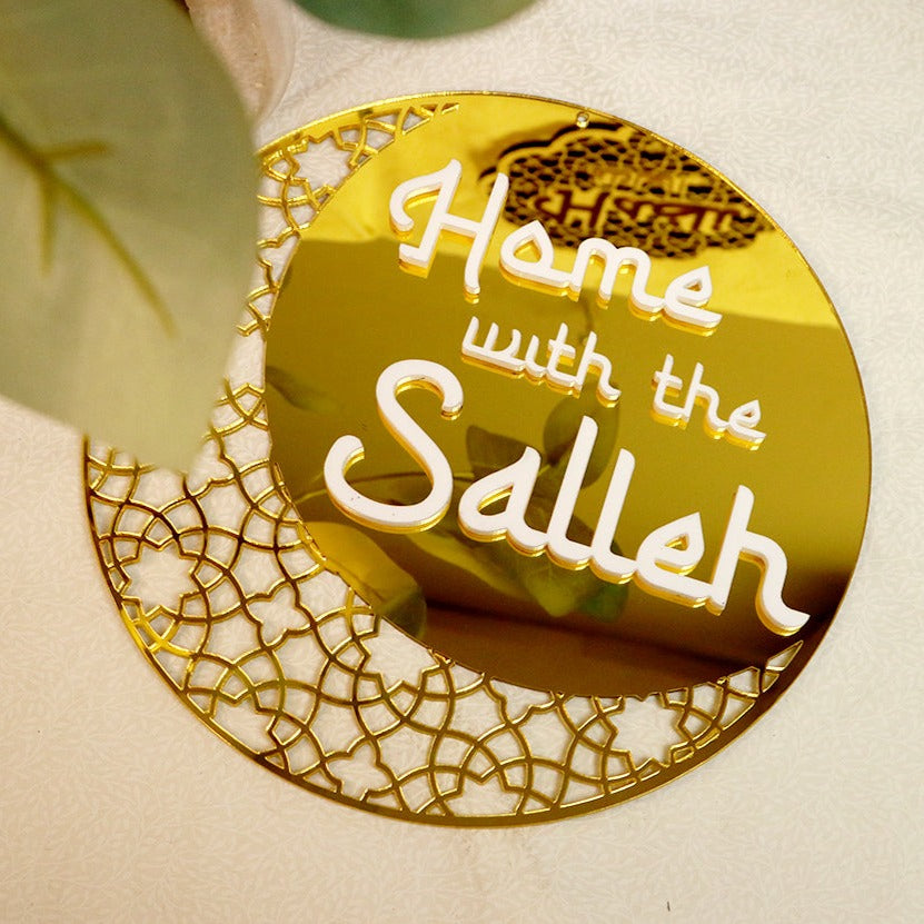 A gold circular hanging ornament with a crescent moon design and the text 'Home with the Salleh' on it.