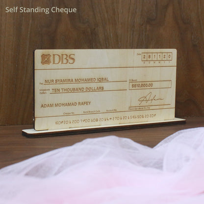 A light wood mock-up cheque with engraved text and signature, resembling a real bank cheque, displayed on a wooden surface.